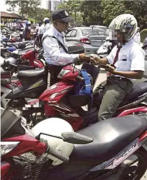  ?? [FOTO IHSAN PDRM] ?? Polis trafik memeriksa lesen memandu pelajar sekolah yang menunggang motosikal di hadapan sebuah sekolah, semalam.