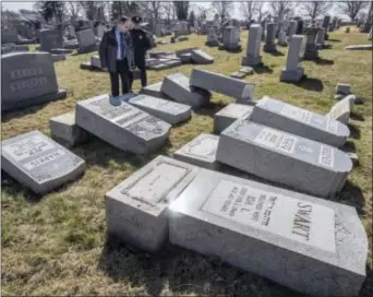  ?? MICHAEL BRYANT — THE PHILADELPH­IA INQUIRER VIA AP ?? Northeast Philadelph­ia Police Det. Timothy McIntyre and another Philadelph­ia police officer look over tombstones that were vandalized in the Jewish Mount Carmel Cemetary Sunday in Philadelph­ia. A police spokeswoma­n said preliminar­y estimates are that...