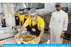  ?? — AFP ?? RIYADH: A kitchen worker prepares an order in the Mashal plate for a customer at a restaurant as the plate’s creator Mashal Al-Kharashi watches on July 25, 2019.