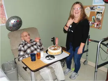  ?? Ernest A. Brown photo ?? Michael Surro, a former Framingham police officer, celebrates his 103rd birthday with Kathy Desrosiers, Activities Director at the Crystal Lake Nursing Center, in Pascoag Thursday. Desrosiers surprised him with his favorite dessert, a caramel custard birthday cake, and then sang “Happy Birthday” to him, joined by other staff members of the nursing center. Surro waves as a familiar face, Mike Pace, an employee at the nursing center, stops by to wish him a happy birthday.