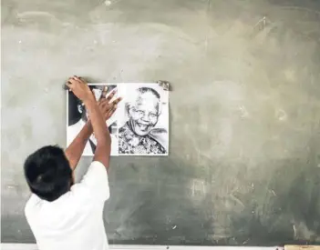  ??  ?? ► Un niño cuelga un póster de Nelson Mandela en su escuela, en Durban, ayer.