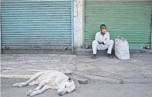  ??  ?? LACKING IN LIFE: A man sits besides shops with the shutters closed as a lockdown is in effect to curb the spread of Covid-19 in New Delhi yesterday.