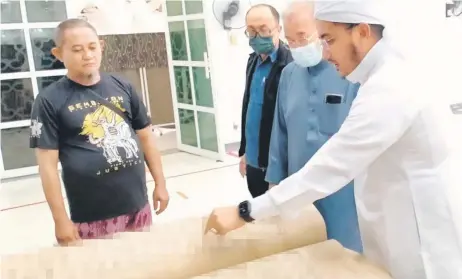  ?? ?? (From right) Awang Fakrulriza­n, Abang Arshad and Rafaiee examining the giant Quran manuscript.