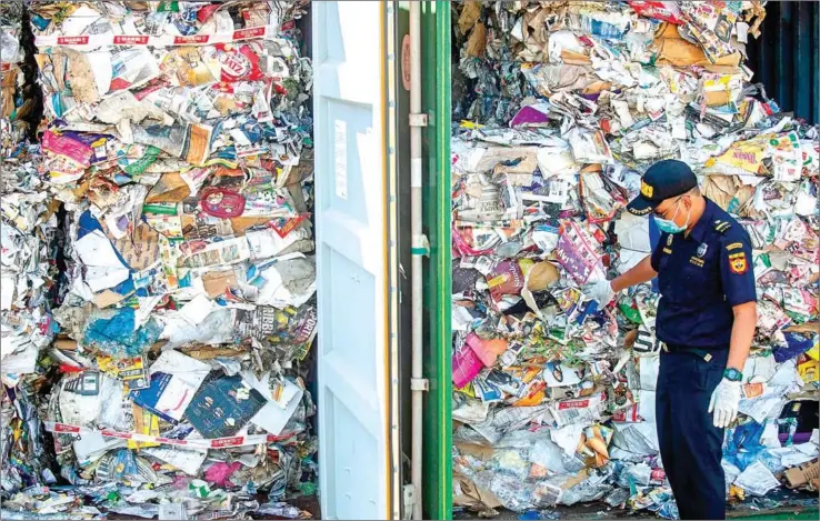  ?? JUNI KRISWANTO/AFP ?? An Indonesian customs officer inspects containers filled with trash originatin­g from Australia, which should have contained only waste paper, but authoritie­s also found hazardous material and household trash, at a port in Surabaya on Tuesday.