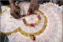  ??  ?? In this file photo, a shopkeeper prepares a garland with Indian 10 Rupees denominati­on notes ($0.15), used particular­ly to garland grooms on their
wedding day, in Jammu, India. (AP)