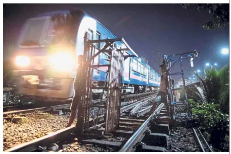  ?? — AFP ?? Risky trade: ‘ Trolley boys’ standing with their home-made carts as they avoid a passing train in Manila.