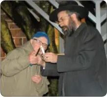  ??  ?? Morris Shenberger of Newtown lights the shamash held by Rabbi Shemtov