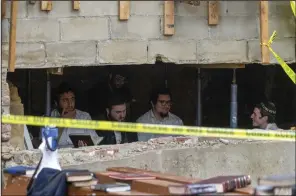  ?? (AP/Bruce Schaff) ?? Hasidic Jewish students sit behind a breach in the wall of a synagogue that led to a tunnel dug by the students. The tunnel was discovered Monday in New York.