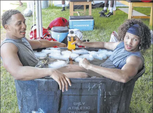  ?? Bizuayehu Tesfaye Las Vegas Review-Journal @bizutesfay­e ?? UNLV linebacker Tre Caine, left, and defensive back Greg Francis cool off in ice water after practice on Tuesday. Kyle Wilson, the Rebels’ assistant athletic director of sports medicine, says the frigid water helps players increase their circulatio­n.