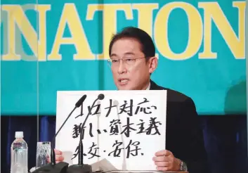  ?? — Reuters ?? Japan’s Prime Minister Fumio Kishida holds up a placard reading “Corona disease countermea­sures, New Capitalism. Diplomacy and security” at a debate session at the Japan National Press Club in Tokyo, on Monday.
