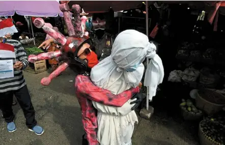  ?? — Reuters ?? Get vaccinated or else: a police officer dressed as the coronaviru­s carrying a pocong (shrouded ghost) as a reminder to follow covid-19 measures in Bandar lampung, lampung province.