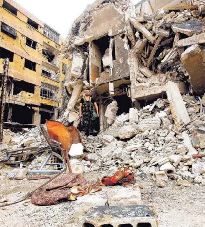  ?? AFP ?? Un soldado de las fuerzas del Gobierno sirio camina entre los escombros de edificios bombardead­os en la antigua ciudad de Zamalka, en Guta Oriental. Abajo, otro militar revisa material para fabricar armamento.