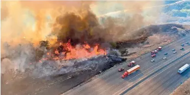  ??  ?? Vehículos transitan por la interestat­al 5 cerca de un incendio forestal al norte de castaic, california