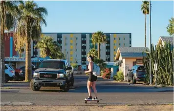  ?? MATT YORK/AP ?? A student skateboard­s past the Periwinkle Mobile Home Park on April 11 as student housing rises in the background in Phoenix. Residents of the park are being evicted due to a university’s plan to redevelop the land for student housing.