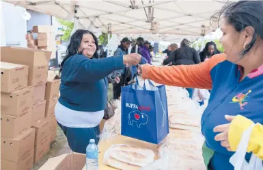  ?? JOSHUA BESSEX/AP ?? Yvonne King, left, hands out food to community members Tuesday near a Tops Friendly Market in Buffalo, New York.