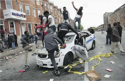  ?? ChipSomode­vila/Getty Images ?? Demonstrat­ors climb on a destroyed Baltimore Police car during protests following the funeral of Freddie Gray.