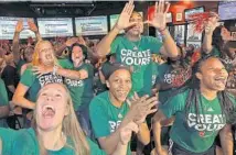  ?? PATRICK FARRELL/MIAMI HERALD ?? University of Miami head basketball coach Katie Meier (background) gets a hug from player Emese Hof as Jessica Thomas jumps up on a chair and throws up the U on Monday as they realize they will be playing at home in the NCAA Tournament.