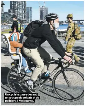  ??  ?? Un cycliste passe devant un groupe de soldats et de policiers à Melbourne.