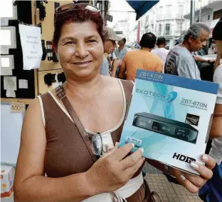  ?? Robson Ventura/Folhapress ?? Helena Clara mostra o conversor digital que comprou por R$ 80 na rua Santa Ifigênia (região central); a professora aposentada pesquisou preços por 2 horas