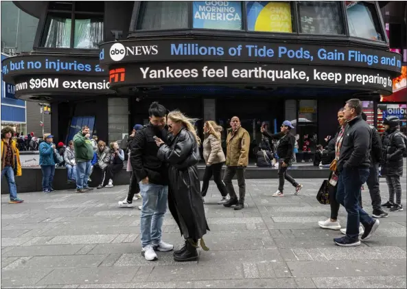  ?? BRITTAINY NEWMAN — THE ASSOCIATED PRESS ?? People walk through Times Square as tickers display news about the East Coast earthquake on Friday in New York.