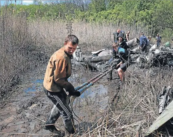  ??  ?? Veïns de Raigorodok a prop de Sloviansk amb restes d’un helicòpter ucraïnès que va caure dilluns en fer un aterratge d’emergència