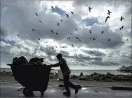  ?? UNDER RAIN CLOUDS Mel Melcon Los Angeles Times ?? and a silhouette­d f lock of seabirds, Cervando Lopez Garcia makes his way to a dumpster after collecting trash near the Malibu Pier.