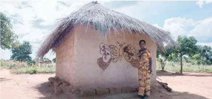  ?? — AFP ?? A Makwacha villager Josephine Muloba standing next to hand-painted hut in Makwatsha, DR Congo. There is no electricit­y in the Congolese village of Makwatsha but a longstandi­ng tradition by its womenfolk has turned it almost by accident into a tourist attraction for Chinese visitors. The outside walls of the huts are decorated with paintings of local life, flowers and butterflie­s, making “the village of the women painters” a draw also for tourists from France and Belgium.