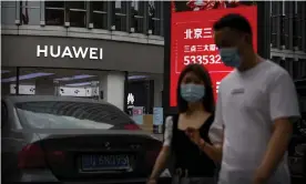  ?? Photograph: Mark Schiefelbe­in/AP ?? People wearing face masks walk past a Huawei store in Beijing, China.