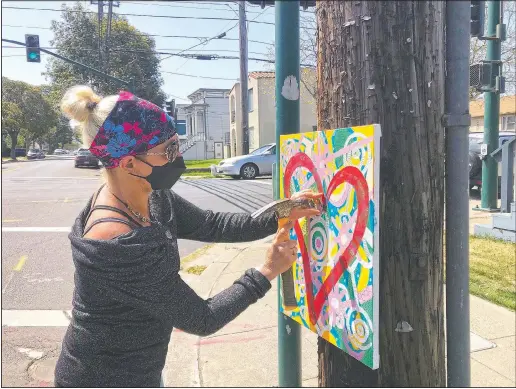  ?? (AP/Janie McCauley) ?? Artist Deirdre Freeman hangs her artwork on a telephone pole in Alameda, Calif. “Hopefully it stays here for a little while,” she says, hammering away as traffic bustles by. “Sometimes cars will beep and wave when they see me doing it.”