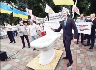  ?? SERGEI SUPINSKY/AFP ?? A protester wearing a mask of Ukrainian President Petro Poroshenko drops symbolic ‘folders with criminal cases’ on corruption­ists down a mock toilet in Kiev on June 17, 2015.