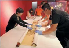  ??  ?? Archaeolog­ists from the Chinese mission that traveled to Greece to help set up the exhibition unroll the portrait of Emperor Qianlong, which greets visitors.