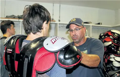  ?? PHOTOS BY BERND FRANKE/WELLAND TRIBUNE ?? Tim Bisci, right, Notre Dame senior football head coach, makes sure Grade 12 student Zac Soos has properly fitting shoulder pads before taking the field for practice.