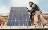  ?? David Maialetti/Philadelph­ia Inquirer ?? John Y.K. Lee moves a solar panel to the edge of his roof in Haverford, Pa.