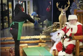  ?? SETH WENIG — THE ASSOCIATED PRESS ?? LaToya Booker cleans a transparen­t barrier between visitors for Santa at a Bass Pro Shop in Bridgeport, Conn. Malls are doing all they can to keep the jolly old man safe from the coronaviru­s, including banning kids from sitting on his knee, completely changing what a Santa visit looks like.