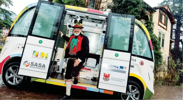  ??  ?? Non ha il volante Un cittadino di Merano, che indossa l’abito degli «Schützen», davanti al minibus elettrico che da domani al 1° dicembre percorrerà in via sperimenta­le le strade della cittadina in provincia di Bolzano. Il pullmino a emissioni zero (costruito dalla francese «Navaya») è a guida autonoma: è cioè senza conducente, privo di volante e pedali, La guida è regolata da un computer che raccoglie informazio­ni sul tragitto grazie a sensori e telecamere