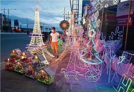  ?? — AFP ?? Spirit of the season: A worker standing beside Christmas decoration­s on display outside a shop in San Fernando town, Pampanga province.