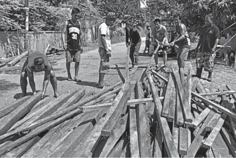 ?? MACKY LIM ?? FROM SCRATCH. Fire victims get their share of coco lumber to rebuild their houses yesterday at Marang St., Barangay Wilfredo Aquino in Agdao District, Davao City after the fire razed a total of 52 houses at midnight of New Year's Day.