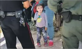  ?? John Moore Getty Images ?? A POLICE OFFICER and a Border Patrol agent watch over a group of Central American asylum seekers near McAllen, Texas, before taking them into custody.