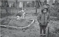  ?? RODRIGO ABD/AP ?? In the courtyard of their house, Vlad, 6, stands near the grave of his mother, who died, on the outskirts of Kyiv, Ukraine on April 4. Vlad's mother died last month when the family was forced to shelter in a basement during the occupation by the Russian army. The family still doesn't know what illness caused her death.