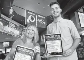  ??  ?? Manager Heather Kammann and server Mike Nolte display the dueling menus at Looney’s Pub. The staff will wear Ravens or Redskins attire today.