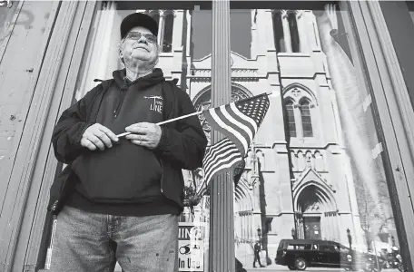  ?? Helen H. Richardson, The Denver Post ?? Jim Moore holds a small American flag as he watches the arrival of the hearse carrying the casket of fallen Boulder police Officer Eric Talley outside the Cathedral Basilica of the Immaculate Conception before Monday’s Mass in Denver.