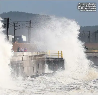  ??  ?? People walk along the harbour in Saltcoats in Ayrshire as high waves
batter the coastline