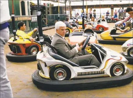  ?? George Rose Getty Images ?? LESLIE NIELSEN, riding a bumper car during a scene for the 1988 film ‘The Naked Gun,’ portrayed a goofball police lieutenant whose investigat­ions lead to even Dodger Stadium and a series of hijinks that parody baseball’s on-field traditions.
