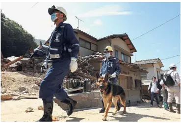  ?? — AFP ?? Not giving up: Members of Japan’s Maritime Self-Defence Forces using a rescue dog to search for missing persons in Kure, Hiroshima prefecture.