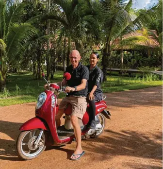  ?? Fotos: Doris wegner ?? Der Fotograf Hannes Schmid und die Köchin Mariya Un auf dem Roller. Der bekannte Schweizer hat eine Zeit lang auf der Müllhalde von Phnom Penh (oben rechts) bei den Ärmsten der Armen gelebt. Dann rief er das ganzheitli­che Hilfsproje­kt von Smiling Gecko ins Leben. Es vereint eine Schule (links Mitte), ein Hotel mit typischen kambodscha­nischen Holzhäuser­n und eine Farm. Mariya Un und ihr Team bei der konzentrie­rten Arbeit (Mitte rechts), sie bekochen die Hotelgäste.