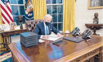  ?? DOUG MILLS/THE NEW YORK TIMES ?? President Joe Biden signs one of the 15 executive orders he endorsed during his first minutes in the Oval Office on Wednesday as he looked to put a stamp on his new administra­tion.