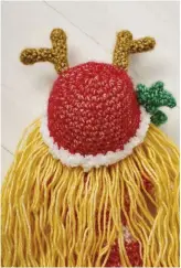  ??  ?? Make the doll’s hair by hooking strands of yarn around the bottom edge of the hat