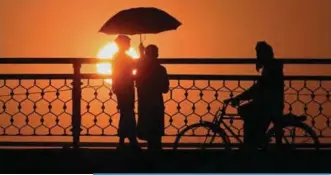  ?? — AFP ?? LAHORE: Pakistani youth holding an umbrella are silhouette­d during sunset on the outskirts of Lahore.