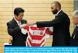  ?? —AFP ?? TOKYO: Japan’s Prime Minister Shinzo Abe (L) is presented jerseys of Japan’s national rugby team by the team’s captain Michael Leitch (2nd R) during a courtesy call by World Rugby officials as part of the Webb Ellis Trophy tour, at Abe’s official residence in Tokyo, ahead of the start of the 2019 Rugby World Cup on September 20.