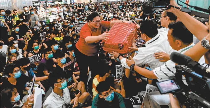  ??  ?? A woman surrounded by pro-democracy protesters passes her luggage to security guards at Hong Kong’s internatio­nal airport this week.